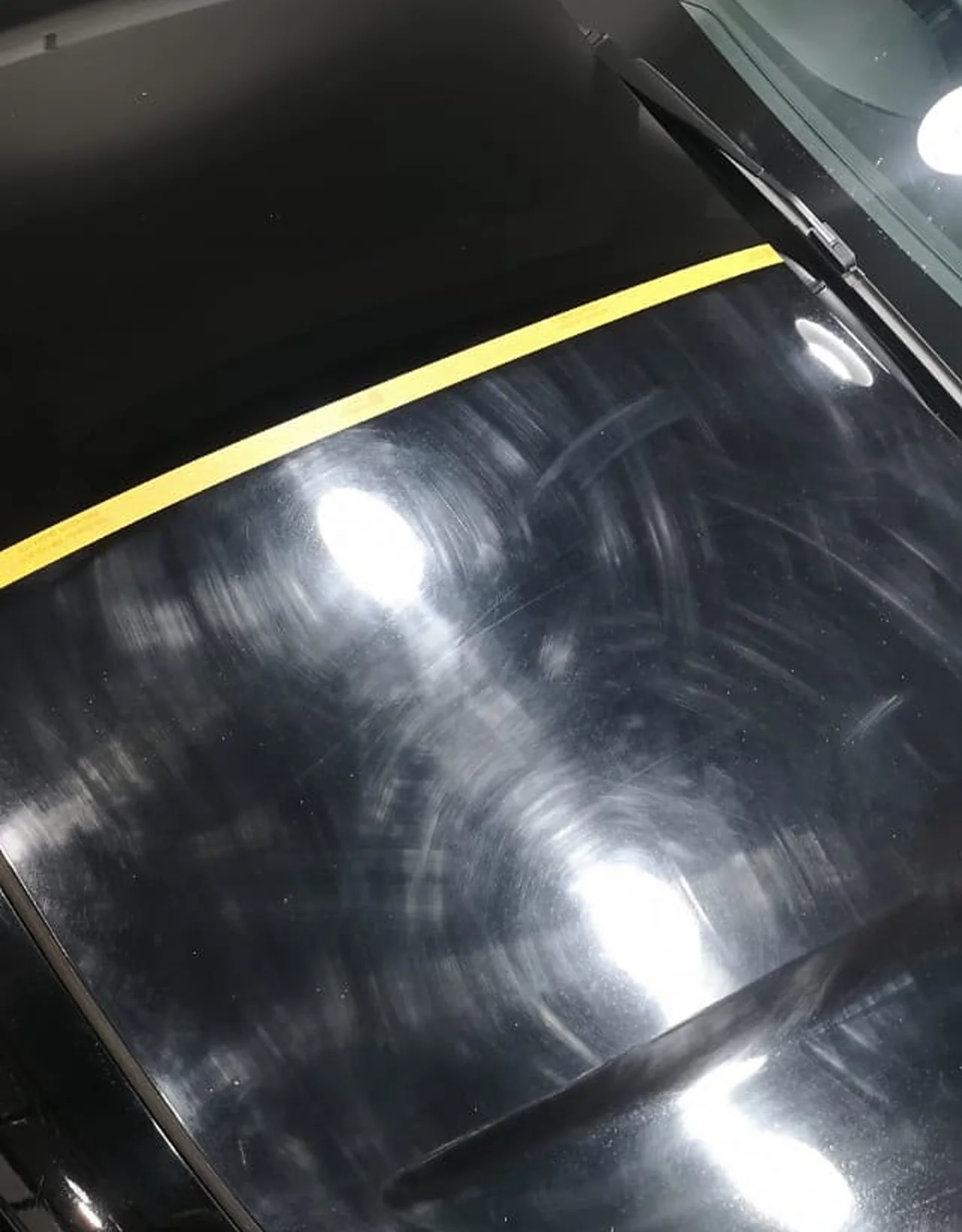 A black Honda HR-V bonnet masked with yellow tape: the polished side reflects cleanly, the untouched side is covered in swirl marks