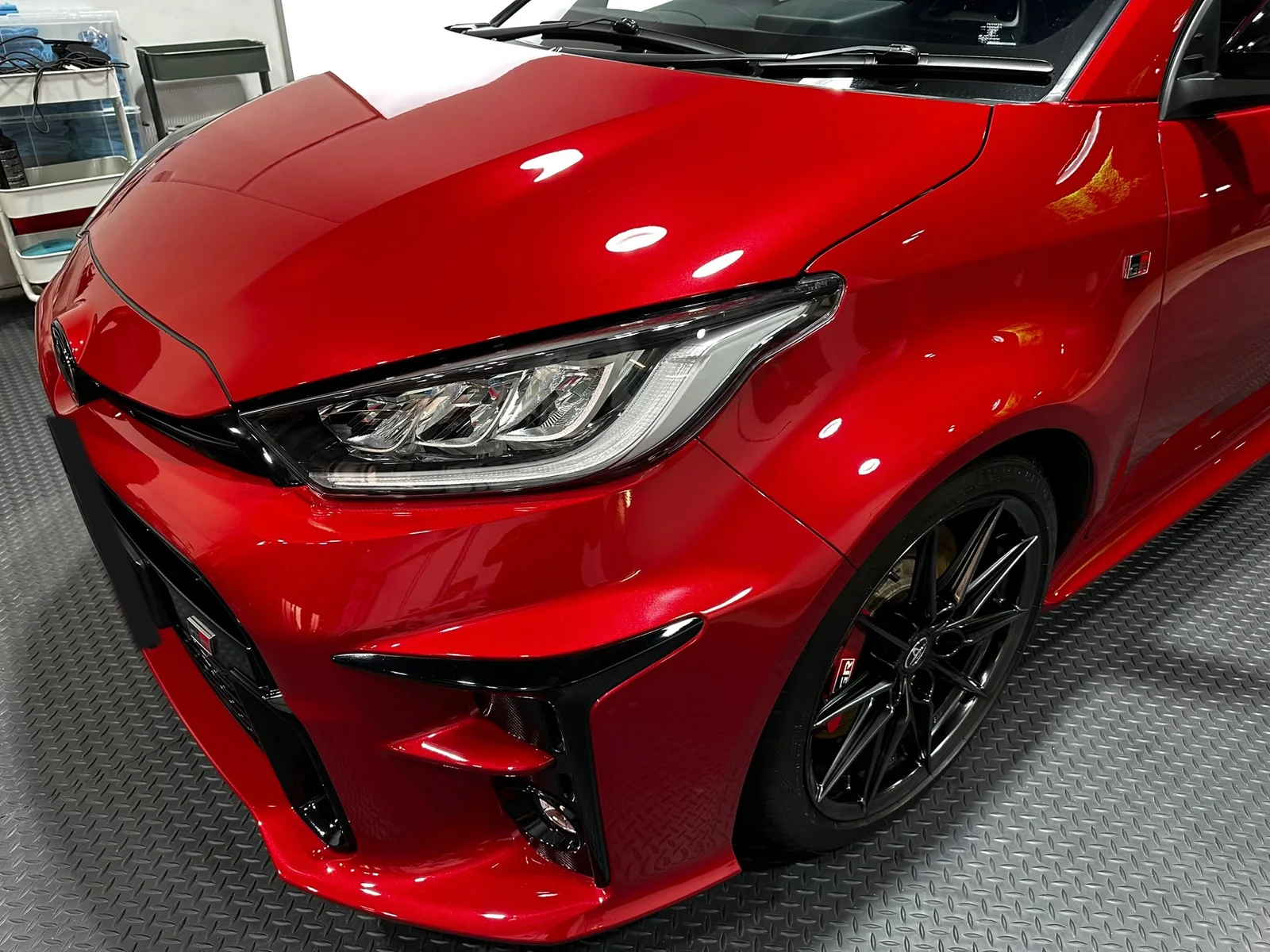 Front three-quarter view of a red Toyota GR Yaris, the bonnet and wing reflecting the studio downlights as clean round points